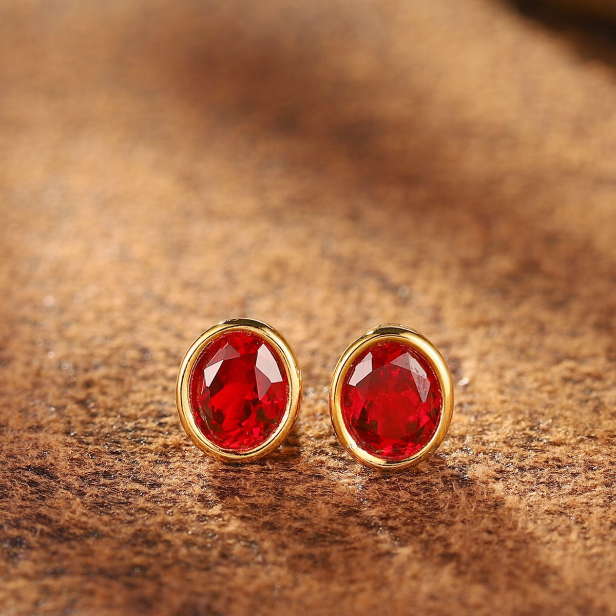 Front view of oval lab-grown ruby bezel stud earrings in 16K gold for everyday elegance