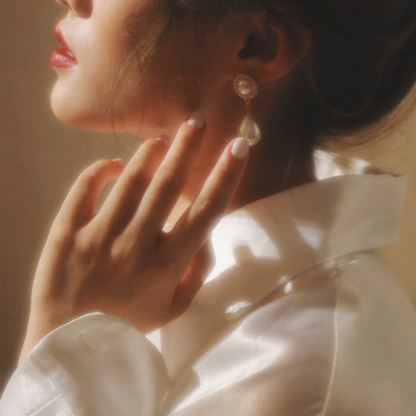 Detail view of teardrop halo high-lustre freshwater pearl earrings for wedding guest looks